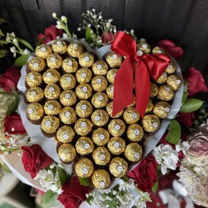 Heart-shaped Ferrero Rocher arrangement with red roses, white flowers, and a red satin bow. A romantic gift for birthdays, anniversaries, quinceañeras, and special celebrations.