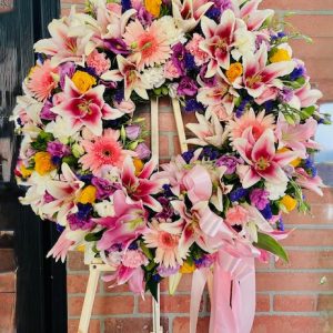 A soft pink and lavender funeral wreath made with lilies, roses, and daisies—crafted to express love, peace, and heartfelt condolences.