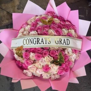 A full, vibrant buchón bouquet made with premium pink and cream roses, accented with gold butterflies and a graduation banner. Bright, fun, and unforgettable for your special grad.